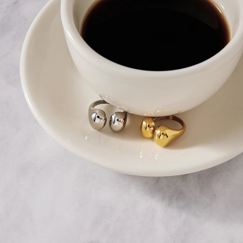 Silver and gold-tone open rings on a saucer beside black coffee