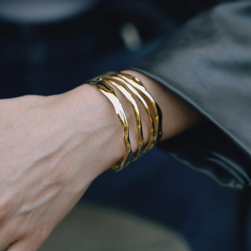 Molten wave cuff worn on a wrist against a dark jacket