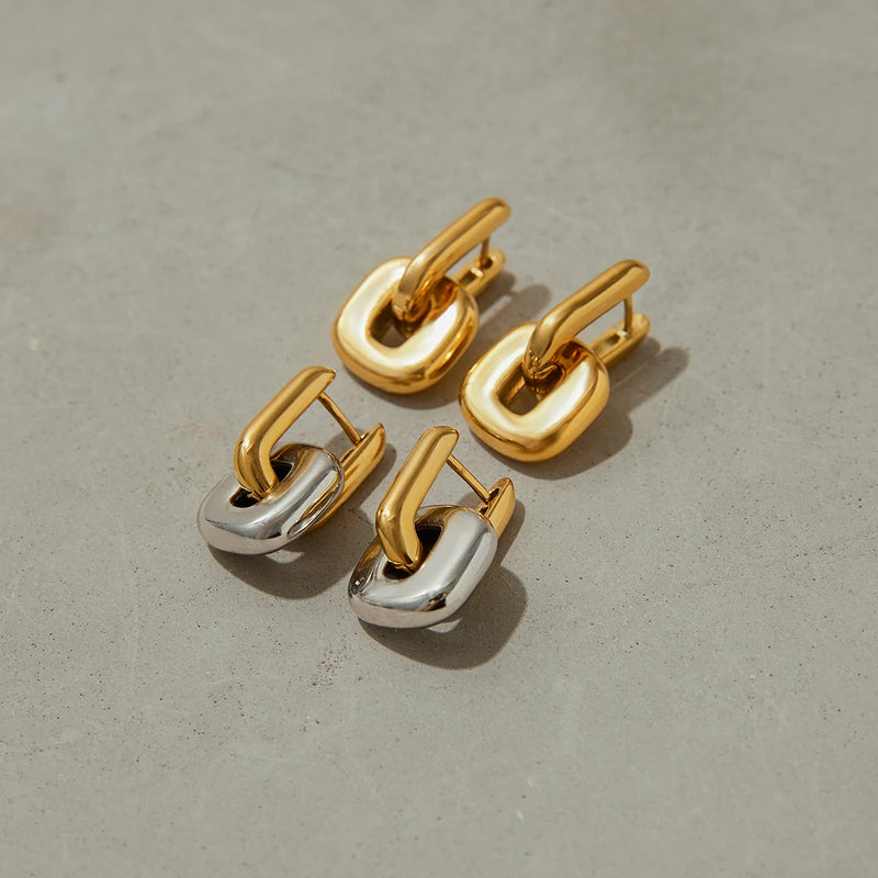 Gold-tone and two-tone link earrings on a pale grey surface