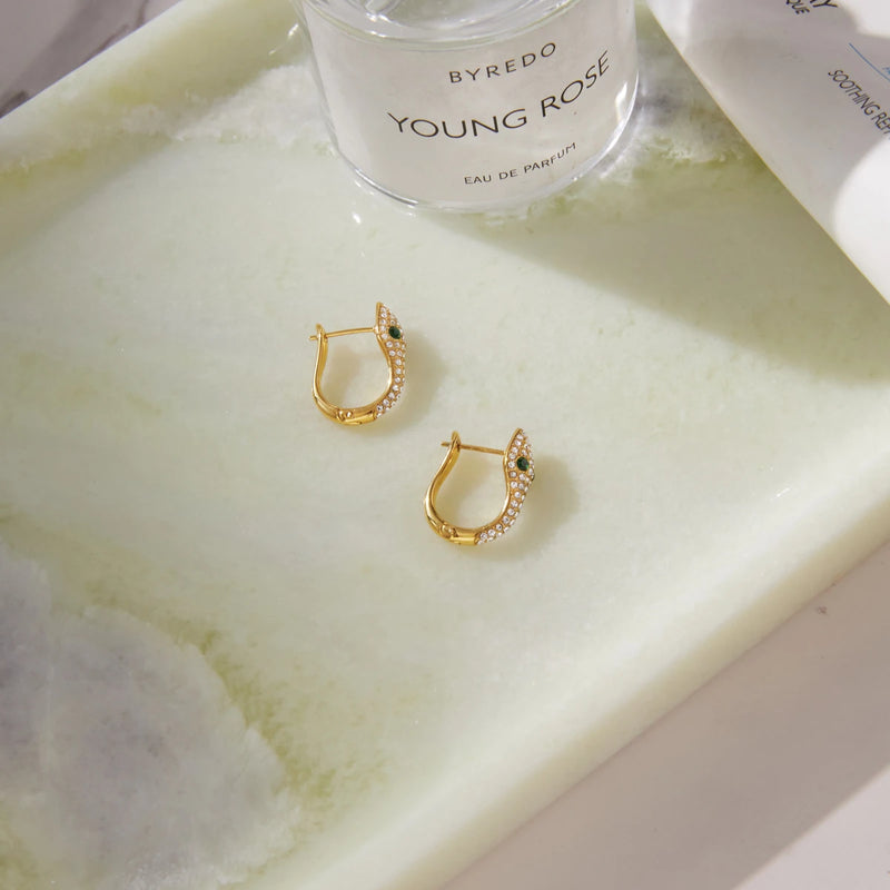Two crystal-set hoops on a pale tray beside a perfume bottle