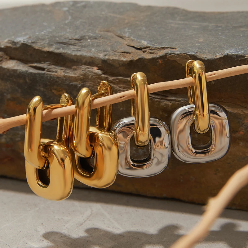 Chunky link earrings hung along a rod against dark stone
