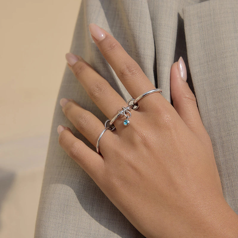 Linked band ring with a blue stone charm worn on a hand