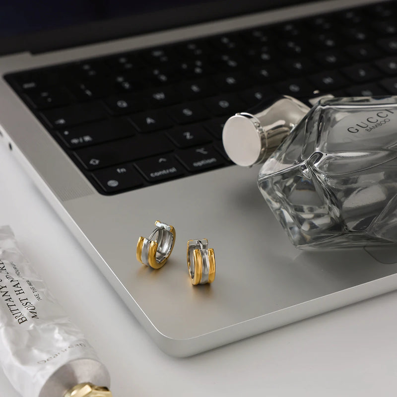 Two pairs of huggie hoops on a laptop beside a glass bottle