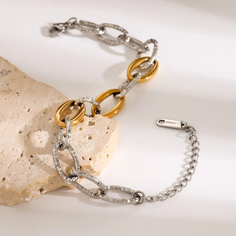Two-tone chain bracelet draped over pale porous stone