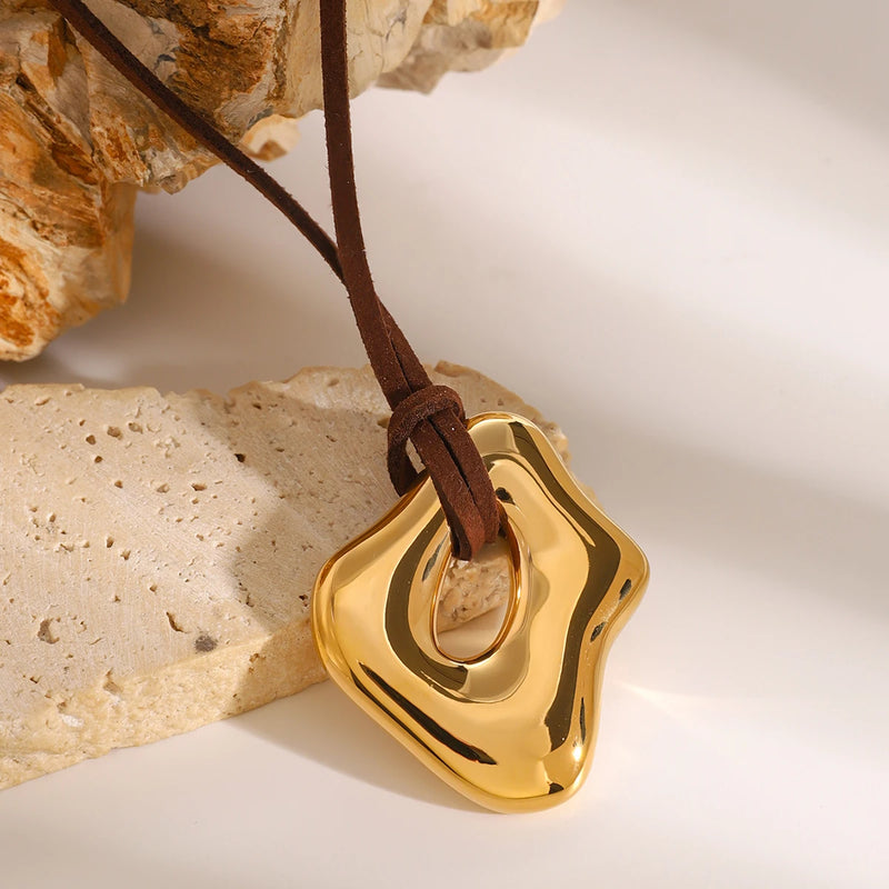 Gold-tone sculptural pendant on a brown cord against stone
