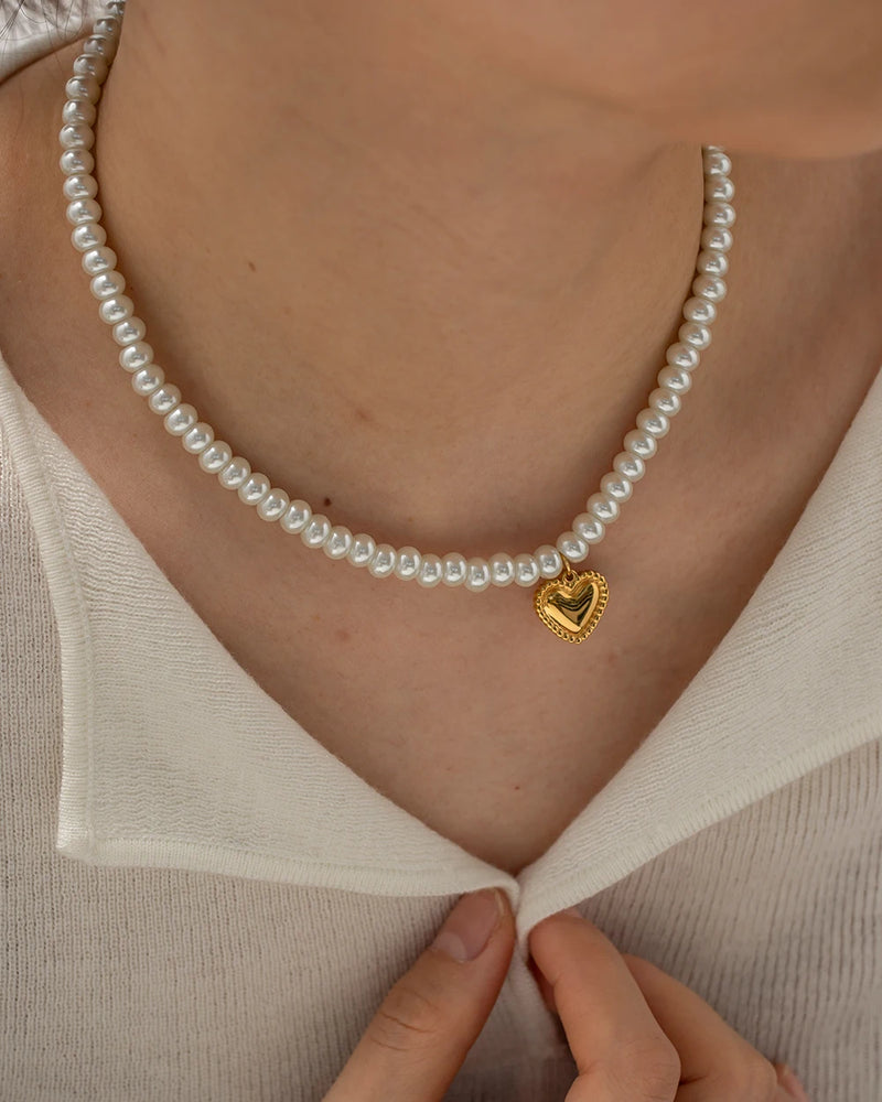Pearl heart necklace worn with a white top, hands at the neckline