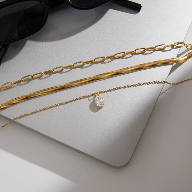 Layered chain necklace laid on a pale surface beside sunglasses
