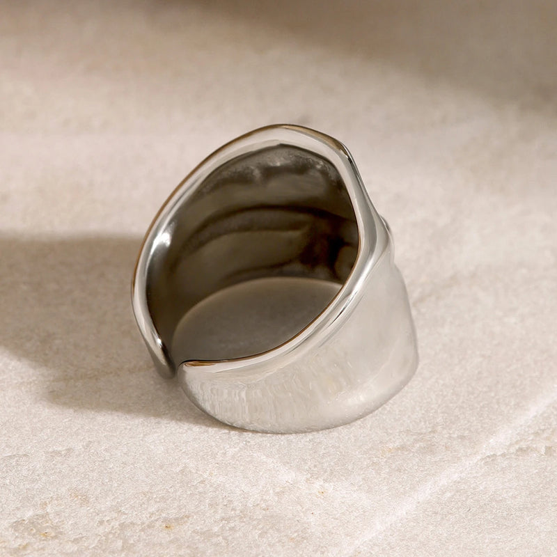 Silver-tone molten wide band ring resting on a pale surface