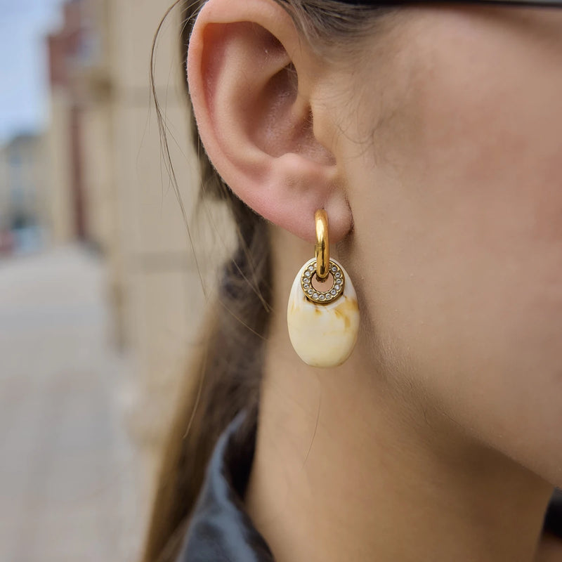 Cream oval resin drop earring worn on the ear