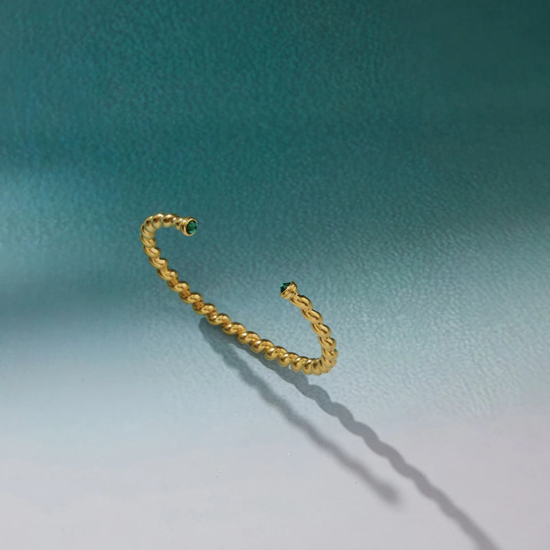 Twisted cuff bangle casting a long shadow on a teal background