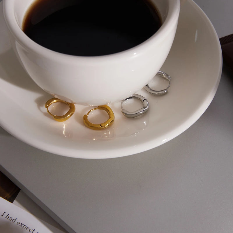 Sculpted hoops in both tones on a saucer beside black coffee