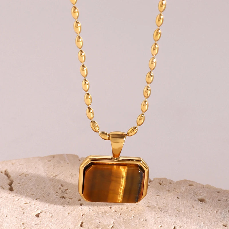 Amber rectangular stone pendant on a chain, propped on stone