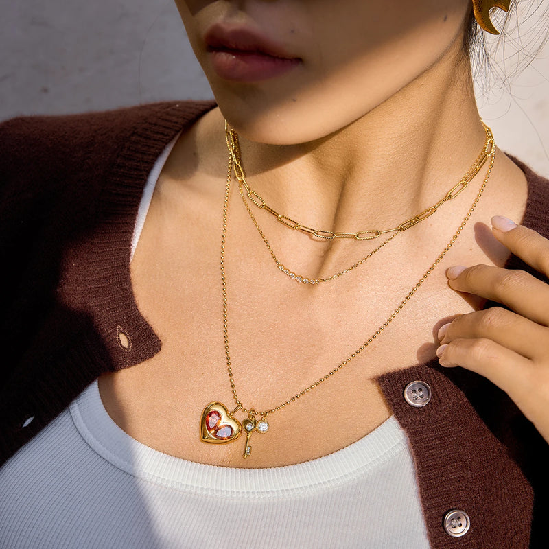 Charm necklace worn layered, hand raised to the shoulder