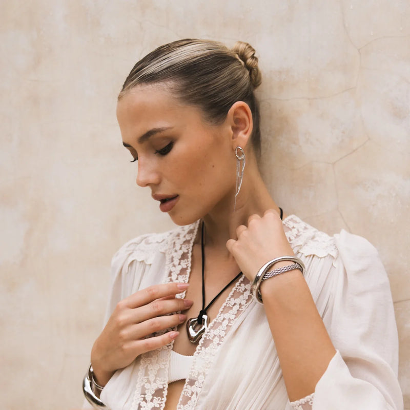 Cord necklace with a sculptural pendant worn, hand at the chest