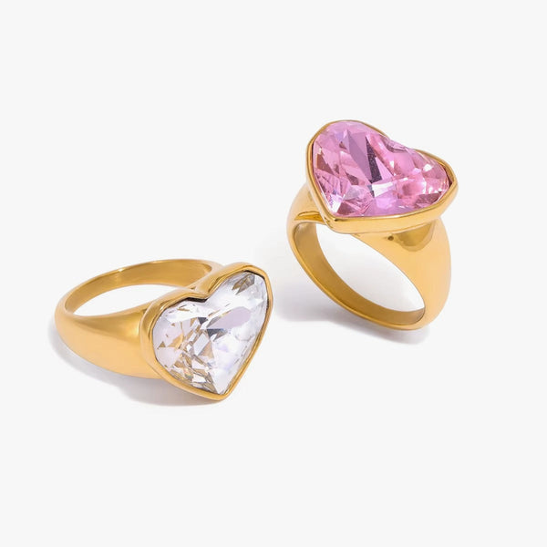 Two heart-set signet rings, one clear crystal and one pink, on white