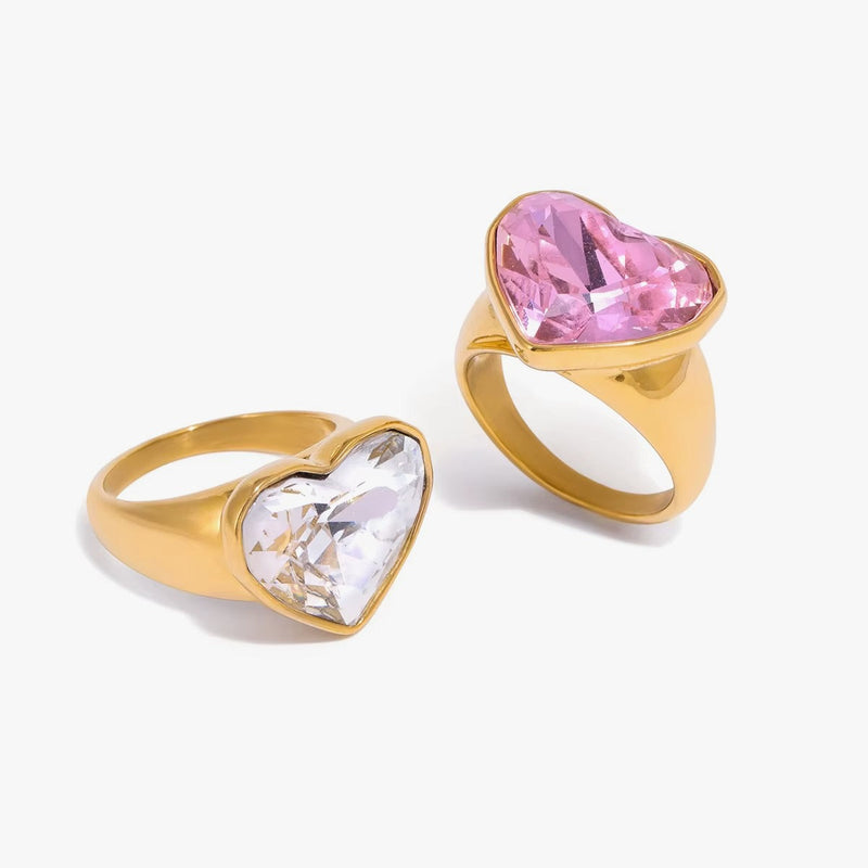 Two heart-set signet rings, one clear crystal and one pink, on white