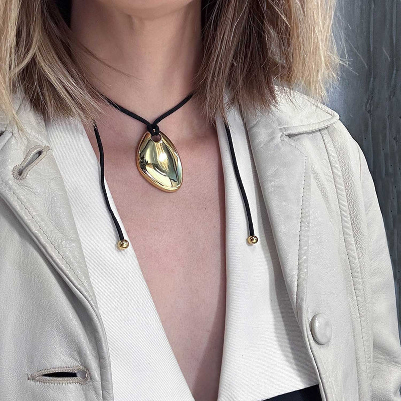 Gold-tone pebble pendant on a cord worn with a cream jacket