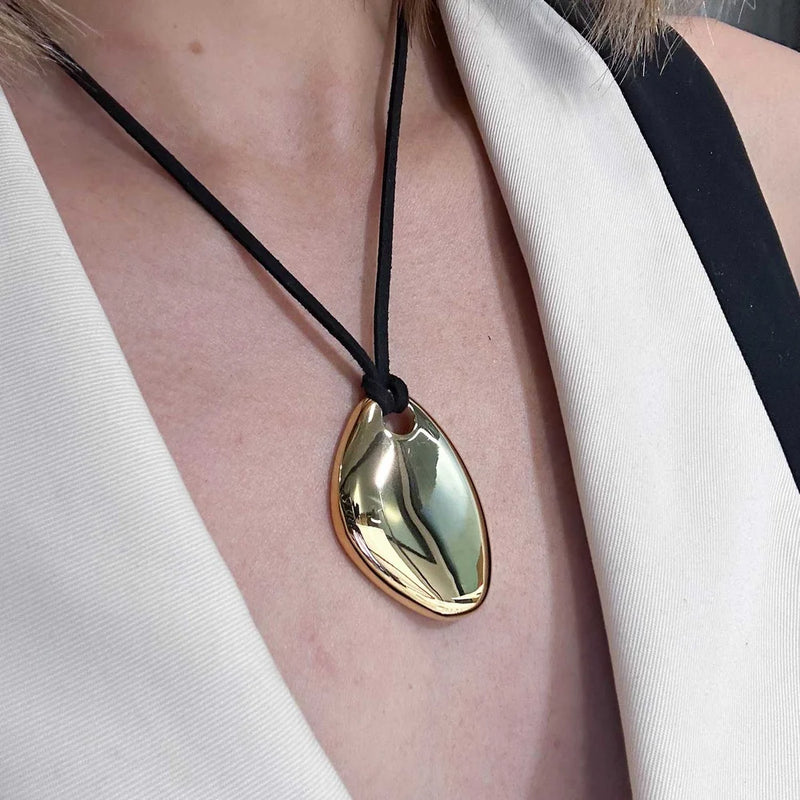 Close view of the gold-tone pebble pendant on a black cord