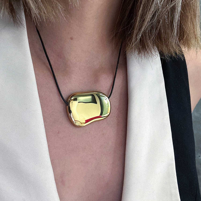 Gold-tone pebble pendant worn against a white collar