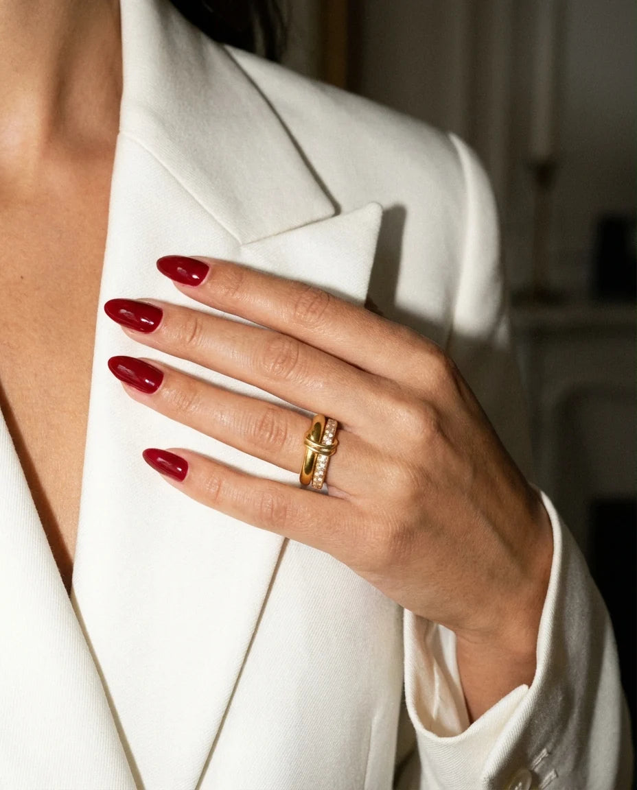 Gold ring with oxblood nails against an ivory lapel