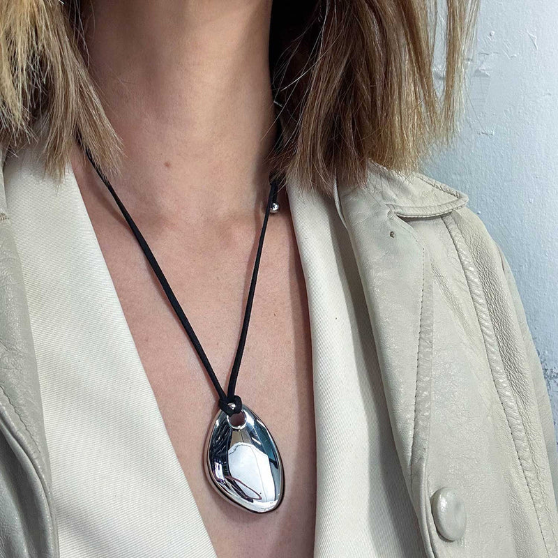 Silver-tone pebble pendant worn with a pale jacket