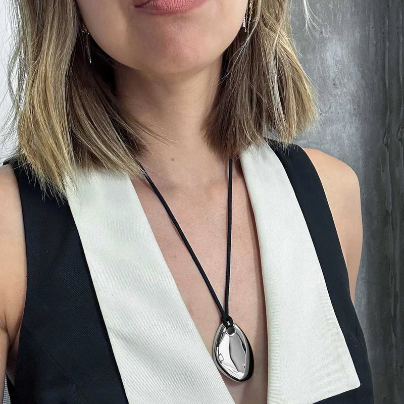 Silver-tone pebble pendant on a cord worn with a black vest