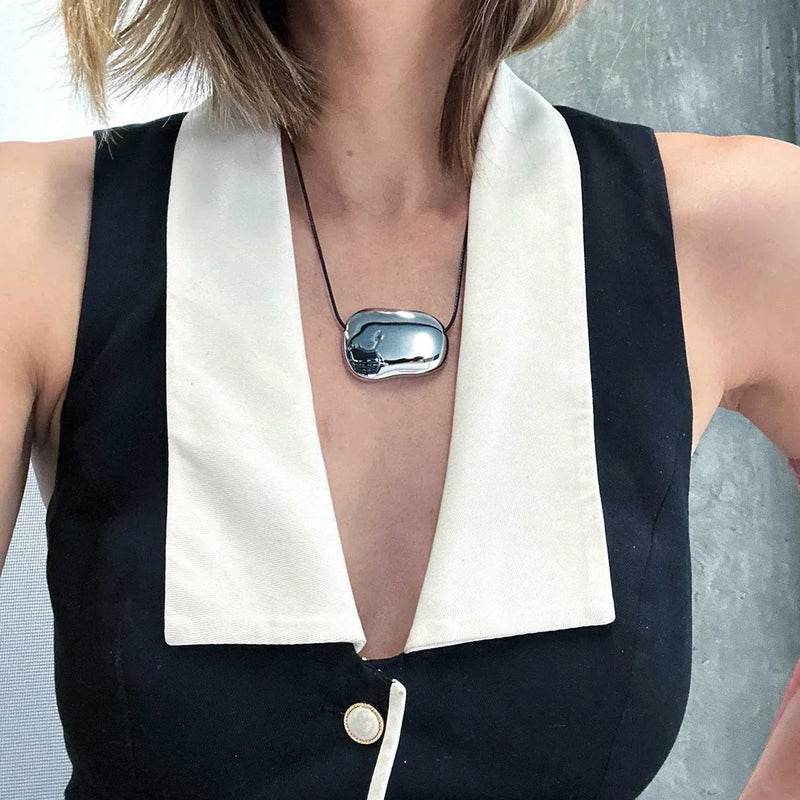 Silver-tone pebble pendant worn with a black and cream vest